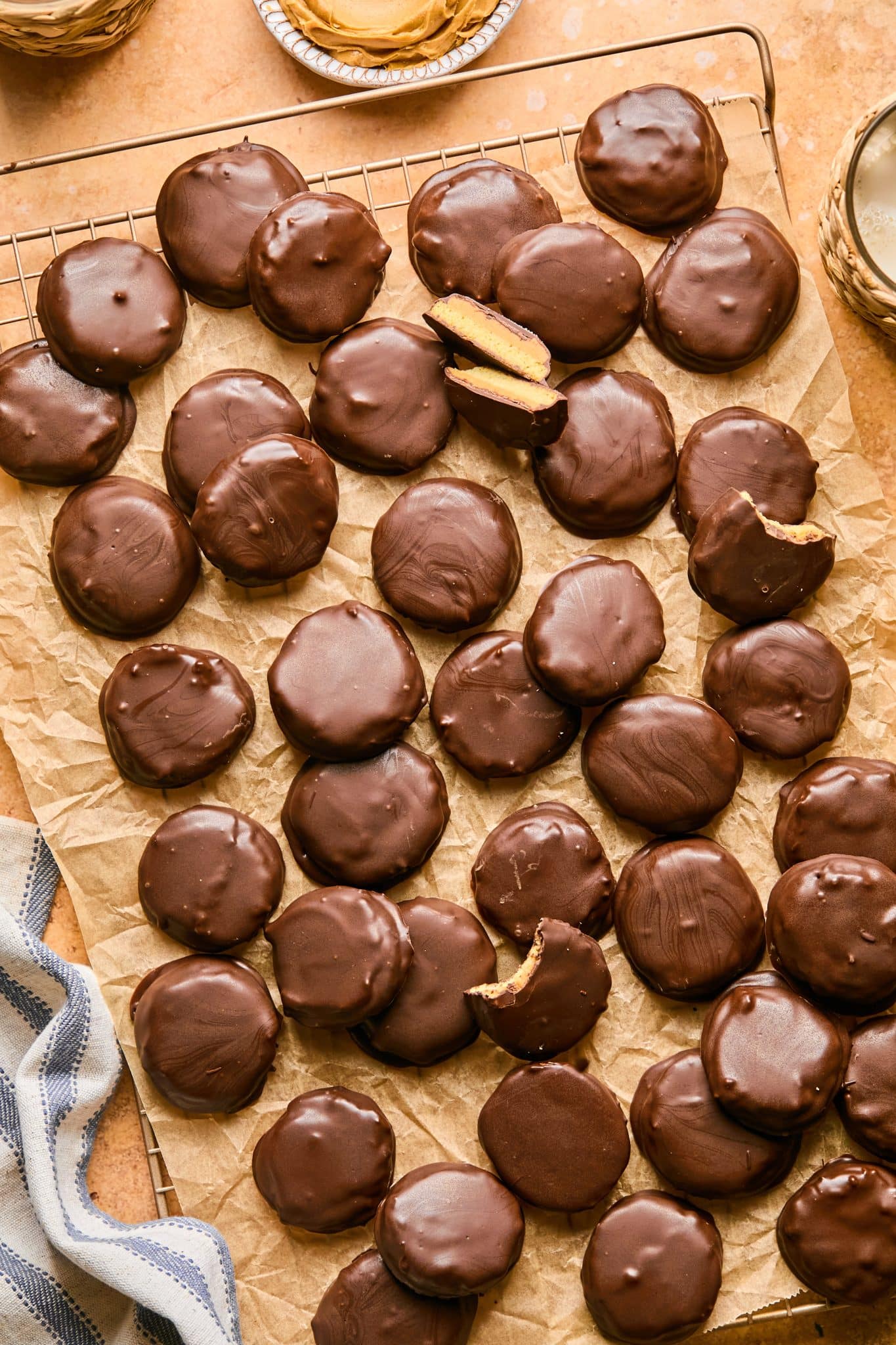 A batch of round, chocolate-coated copycat Tagalong cookies arranged on crinkled parchment paper, with a couple cookies partially bitten to reveal its golden peanut butter filling.
