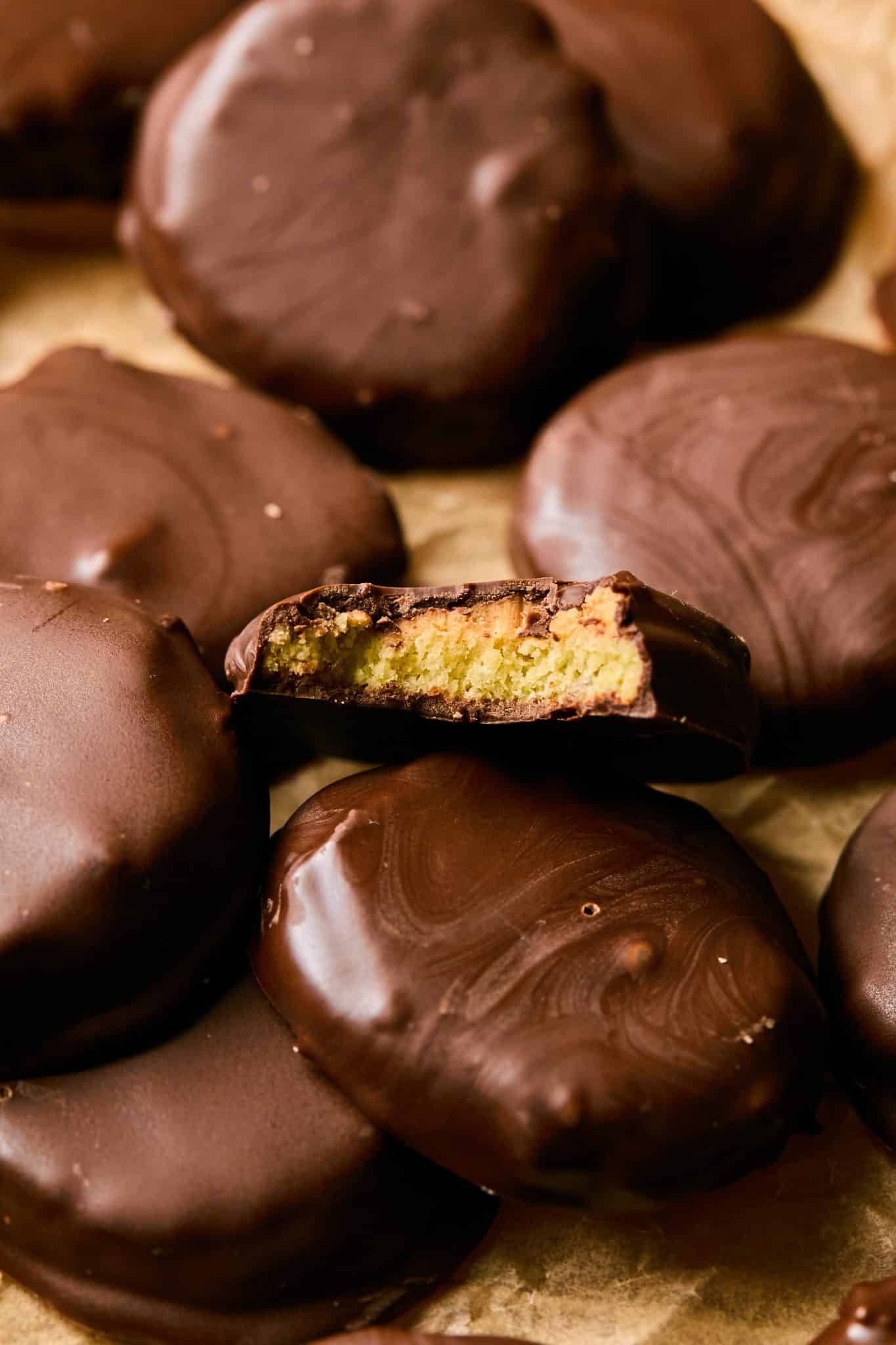 A stack of homemade Tagalong cookies coated in glossy chocolate, with one cookie bitten to reveal the golden peanut butter filling inside.



